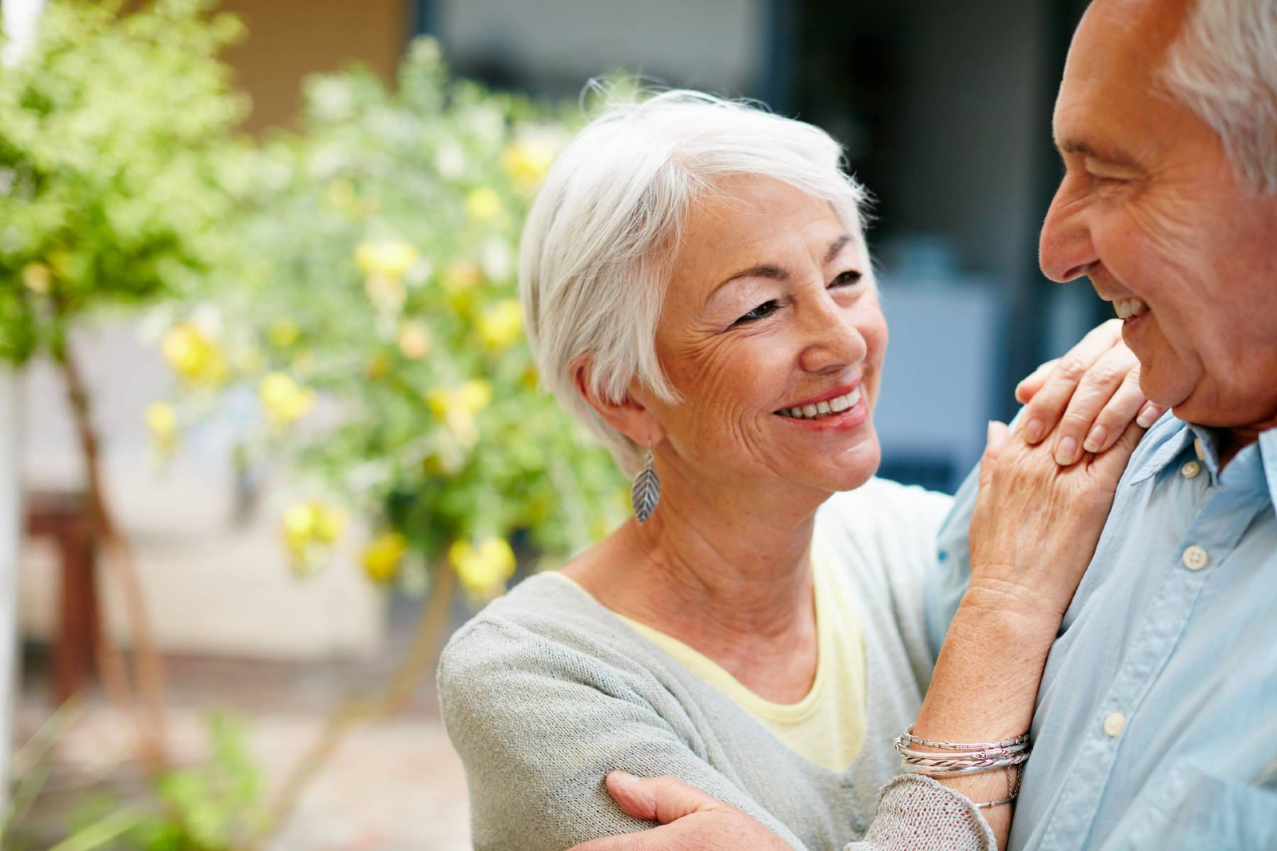 A senior woman clasps her hand and rests them on her husband's shoulders