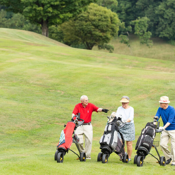 Three seniors rolling their bags on the golf course