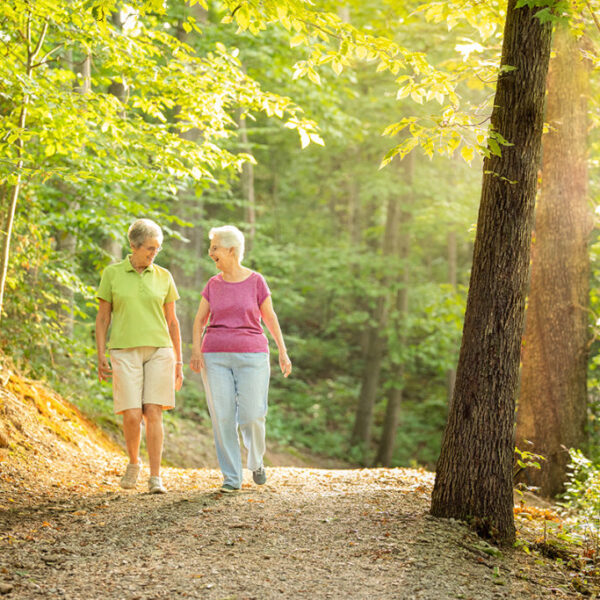 Two senior women talking a stroll on a walkway in the forest