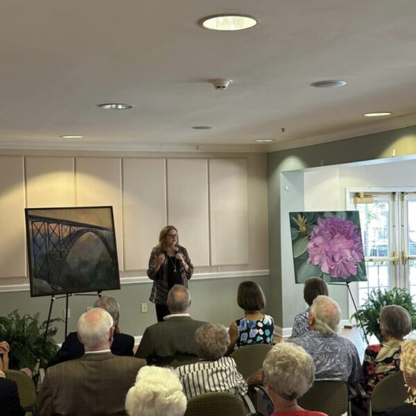 A staff member explaining the painting with the bridge at the Newt and Nancy Thomas gallery