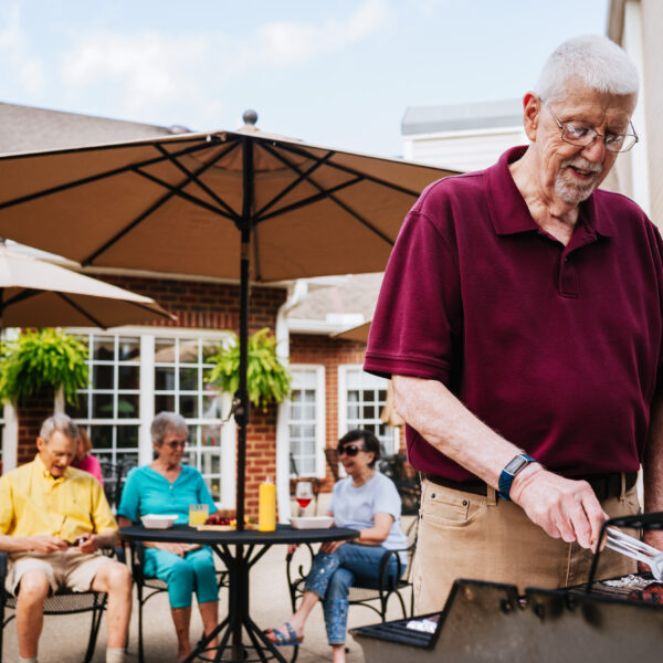 A male resident grilling hotdogs for other residents in the patio