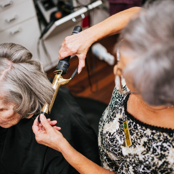 A resident getting her hair curled by another resident at the community salon