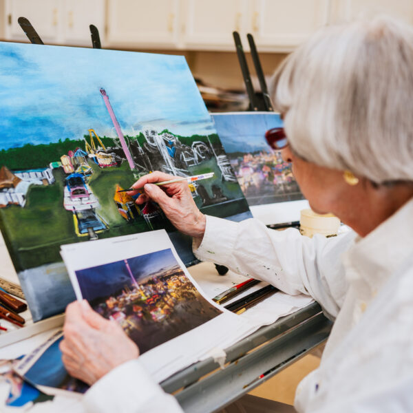 Resident painting a still-life of a photograph of a carnival