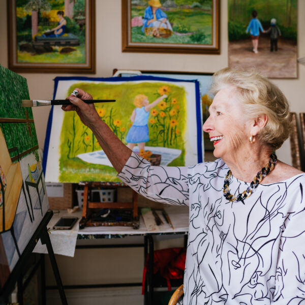 A senior resident painting and displaying her many different paintings