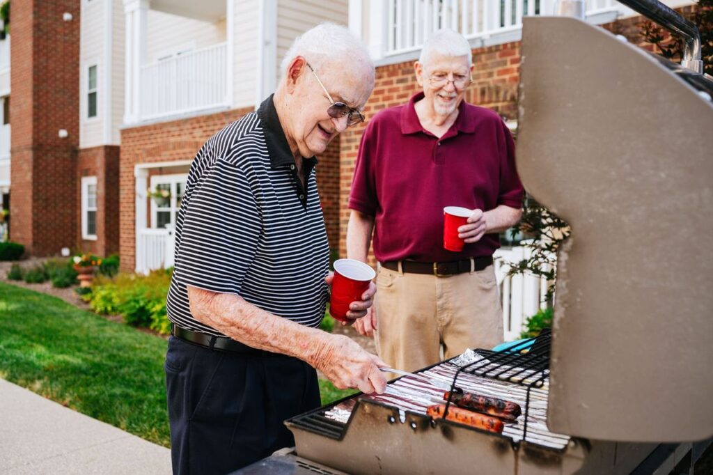 Two senior men socializing, as man is grilling hot dogs