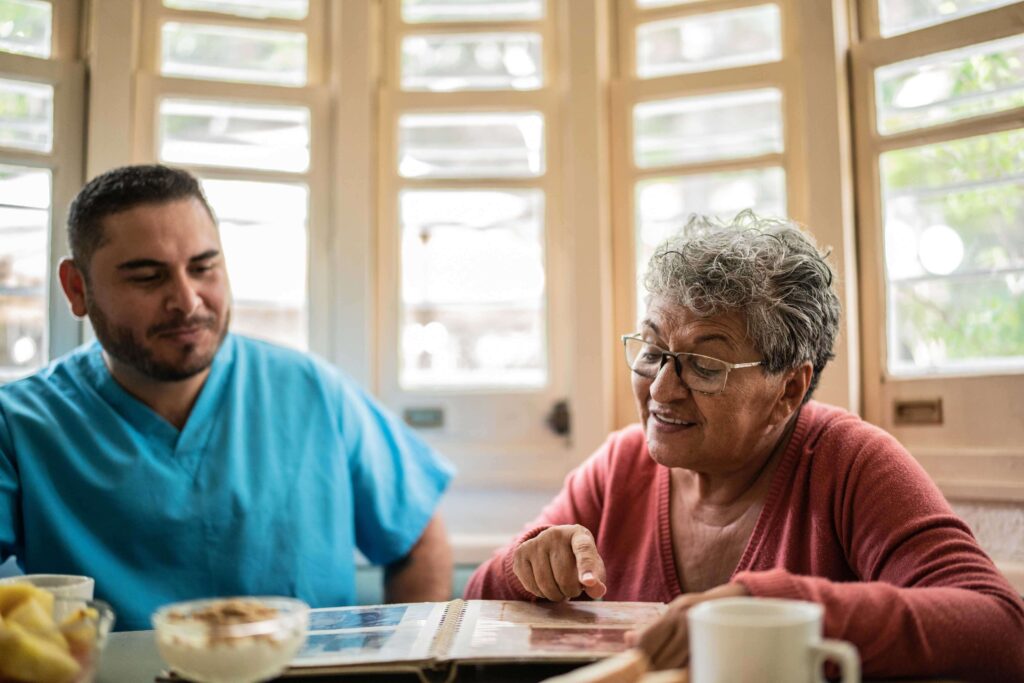 Senior woman and her nurse looking at a photo album in the dining room together