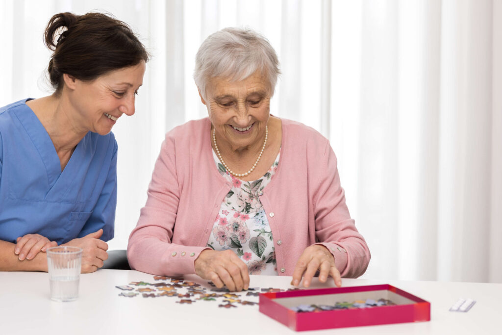 A senior woman completing a jigsaw puzzle with her caregiver