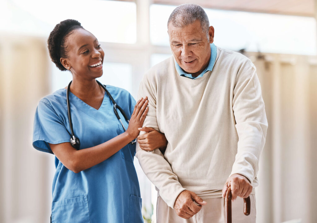 A caregiver helping an elderly man walk with a cane